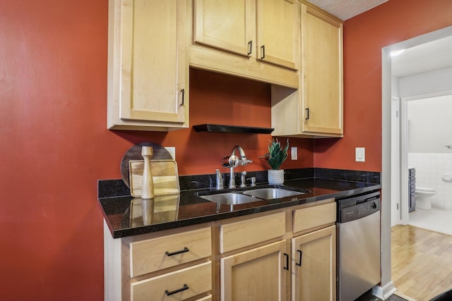 kitchen featuring stainless steel dishwasher, sink, light brown cabinets, dark stone countertops, and hardwood / wood-style floors