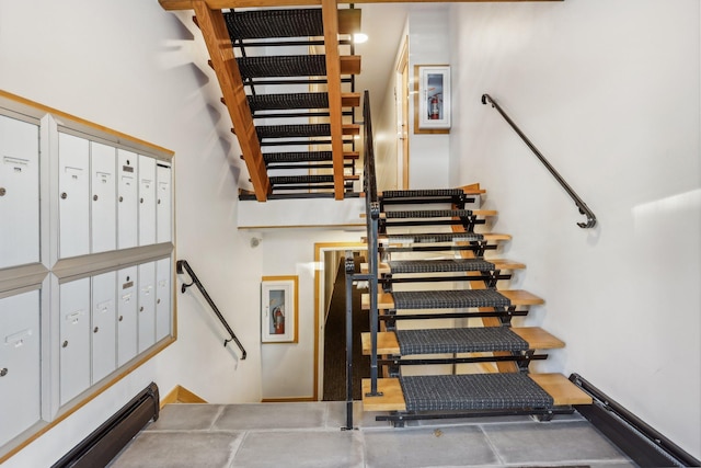 staircase featuring a towering ceiling, a baseboard radiator, and a mail area