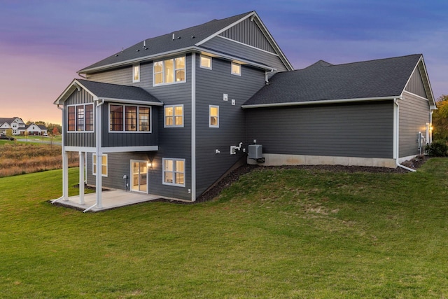 back house at dusk featuring central AC, a lawn, and a patio