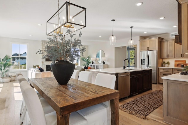 kitchen with sink, hanging light fixtures, appliances with stainless steel finishes, a fireplace, and a kitchen island with sink