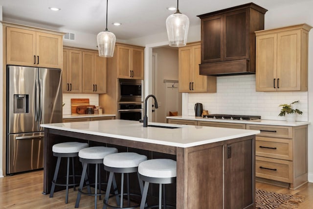 kitchen with stainless steel appliances, sink, decorative light fixtures, and a kitchen island with sink