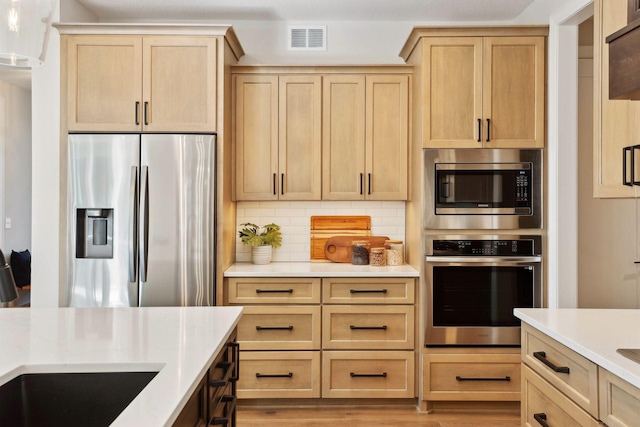 kitchen with stainless steel appliances, light brown cabinetry, light hardwood / wood-style floors, and backsplash