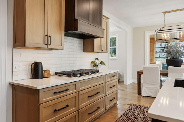 kitchen featuring backsplash, a chandelier, hanging light fixtures, stainless steel gas cooktop, and light hardwood / wood-style flooring