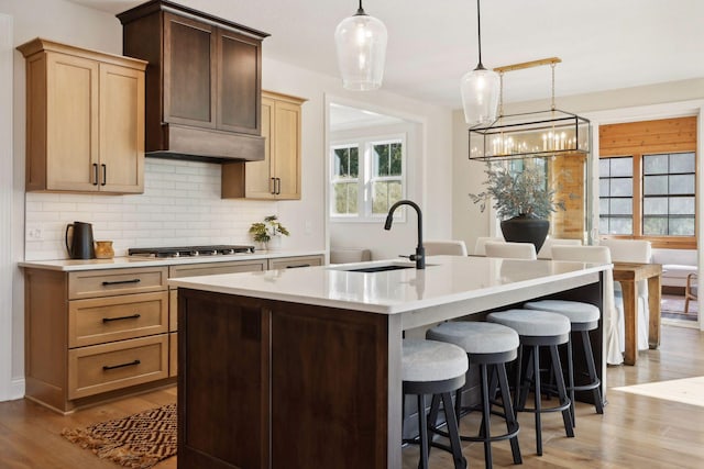 kitchen featuring a kitchen bar, sink, an island with sink, pendant lighting, and backsplash