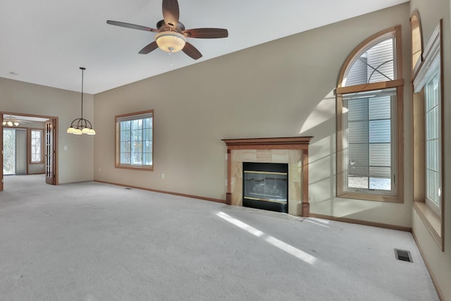 unfurnished living room featuring ceiling fan with notable chandelier, light colored carpet, and a fireplace