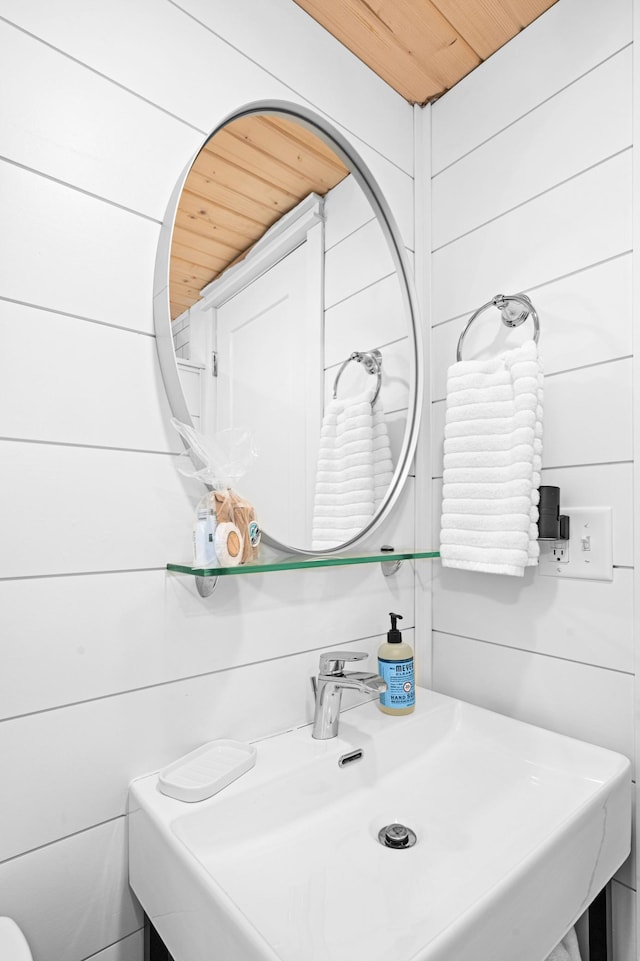 bathroom featuring wooden walls, wooden ceiling, and sink