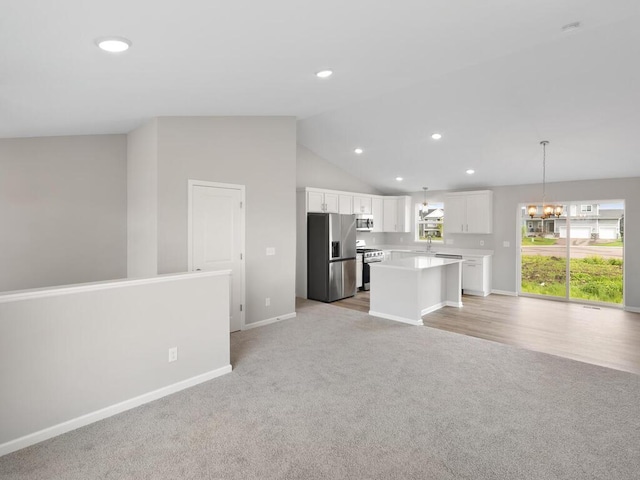 kitchen with stainless steel appliances, decorative light fixtures, white cabinetry, lofted ceiling, and a kitchen island