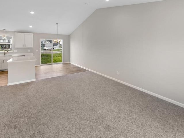 unfurnished living room featuring sink, vaulted ceiling, light carpet, and a chandelier