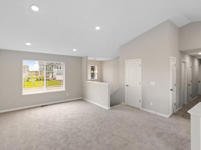 carpeted spare room with vaulted ceiling and a notable chandelier