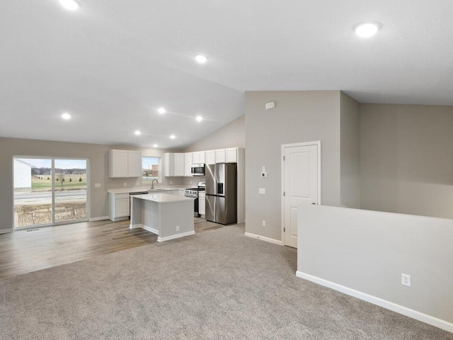 kitchen with appliances with stainless steel finishes, sink, white cabinets, a center island, and light carpet