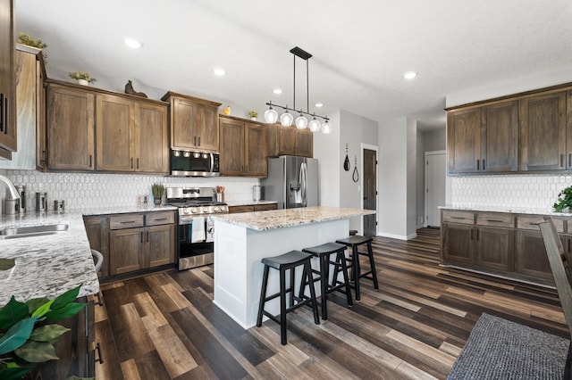 kitchen with pendant lighting, a center island, sink, light stone countertops, and stainless steel appliances