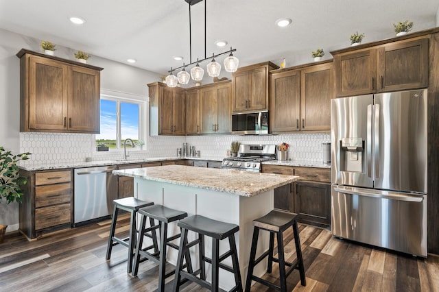 kitchen with appliances with stainless steel finishes, dark hardwood / wood-style flooring, sink, decorative light fixtures, and a kitchen island