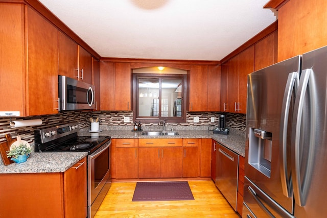 kitchen with appliances with stainless steel finishes, sink, dark stone countertops, decorative backsplash, and light hardwood / wood-style flooring