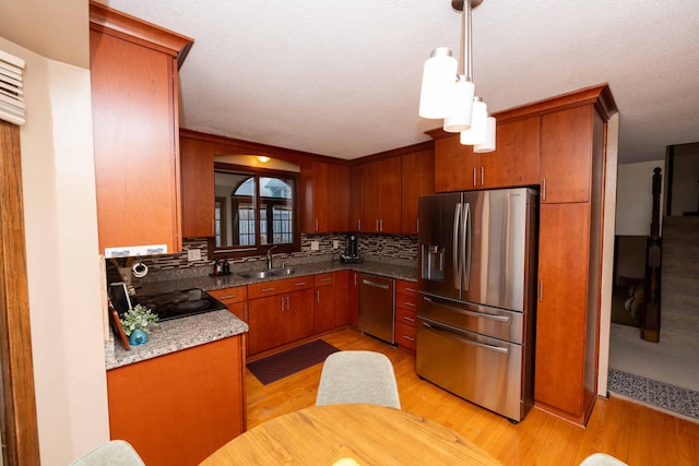 kitchen with tasteful backsplash, sink, hanging light fixtures, stainless steel appliances, and light hardwood / wood-style flooring