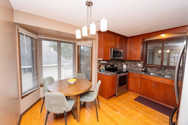 kitchen featuring sink, decorative backsplash, hanging light fixtures, stainless steel appliances, and light wood-type flooring