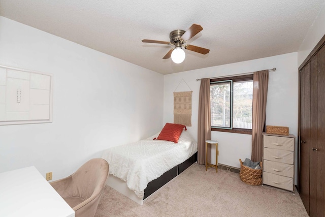 bedroom with ceiling fan, light colored carpet, a textured ceiling, and a closet