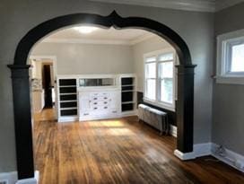 unfurnished living room featuring radiator, dark wood-type flooring, and a healthy amount of sunlight