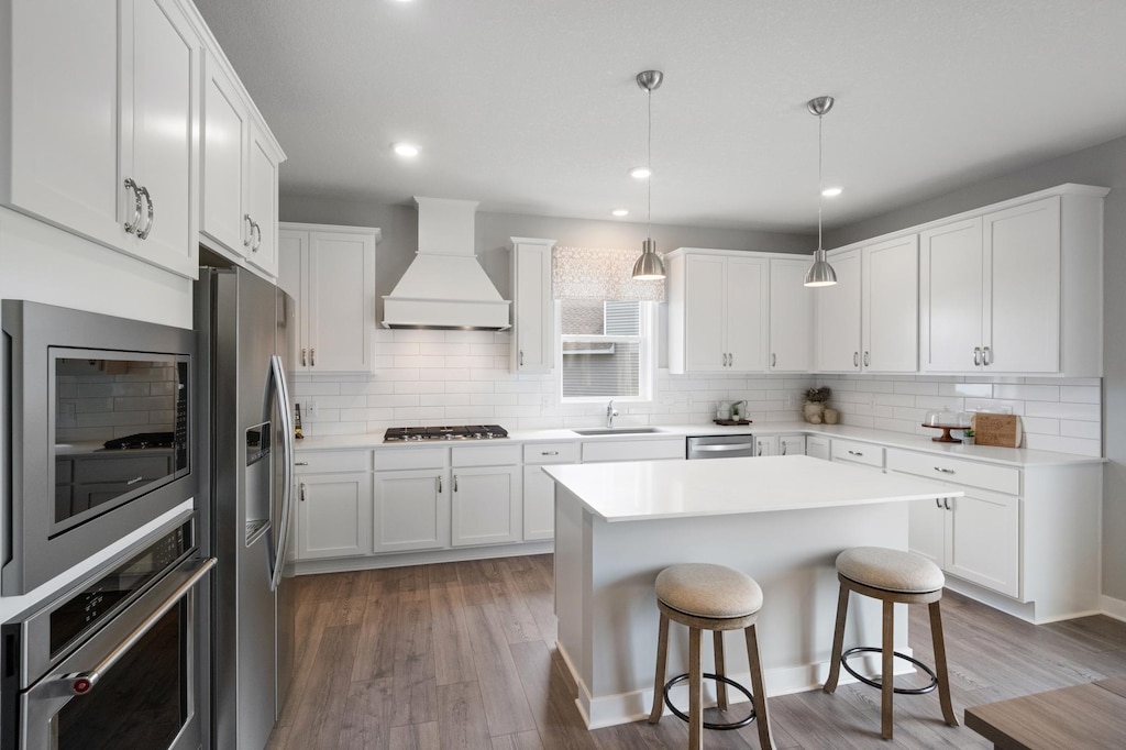 kitchen featuring decorative light fixtures, white cabinetry, custom range hood, and stainless steel appliances