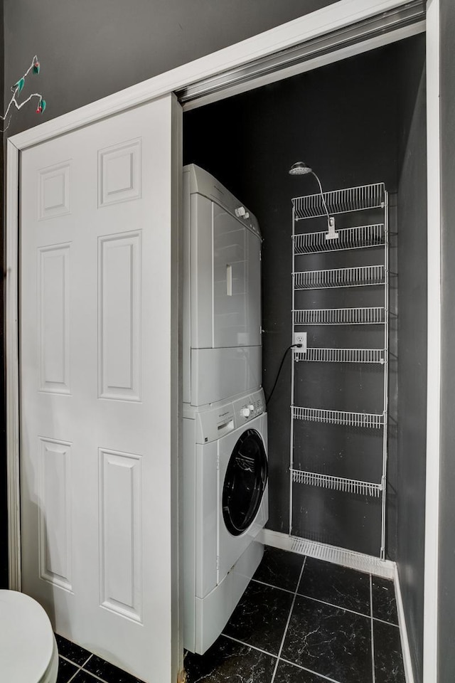 laundry room with dark tile patterned floors and stacked washer and clothes dryer