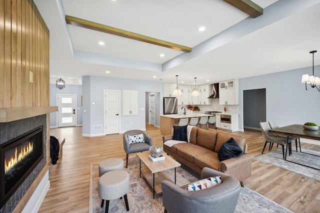 living room with an inviting chandelier, light hardwood / wood-style floors, beam ceiling, and a tiled fireplace