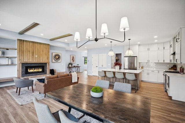 dining area featuring a large fireplace, light wood-type flooring, and beam ceiling