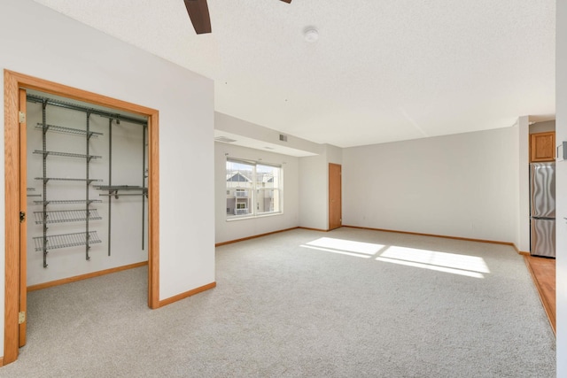 unfurnished living room with ceiling fan, light colored carpet, and a textured ceiling