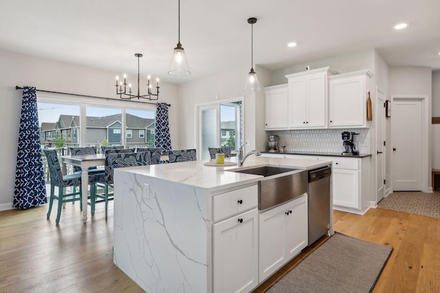 kitchen featuring stainless steel dishwasher, white cabinets, a kitchen island with sink, and hanging light fixtures