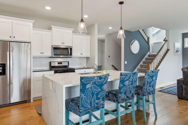 kitchen with white cabinetry, stainless steel appliances, an island with sink, pendant lighting, and a breakfast bar area