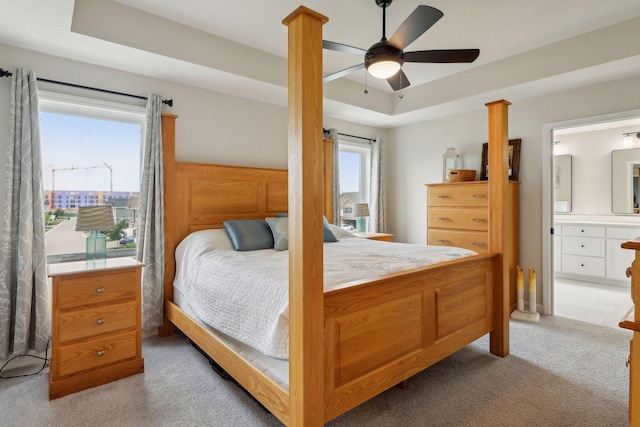 carpeted bedroom featuring ensuite bathroom, a raised ceiling, and ceiling fan