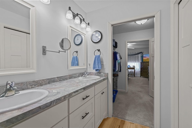 full bathroom featuring double vanity, a textured ceiling, a sink, and wood finished floors