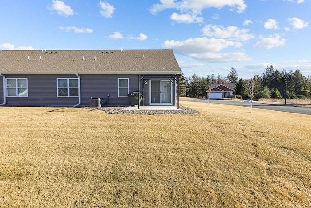 back of property with cooling unit, roof with shingles, and a lawn