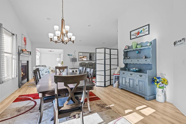 dining space featuring baseboards, light wood-type flooring, a glass covered fireplace, and a notable chandelier