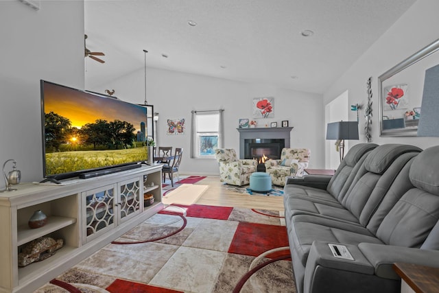 living area with a ceiling fan, vaulted ceiling, wood finished floors, and a glass covered fireplace