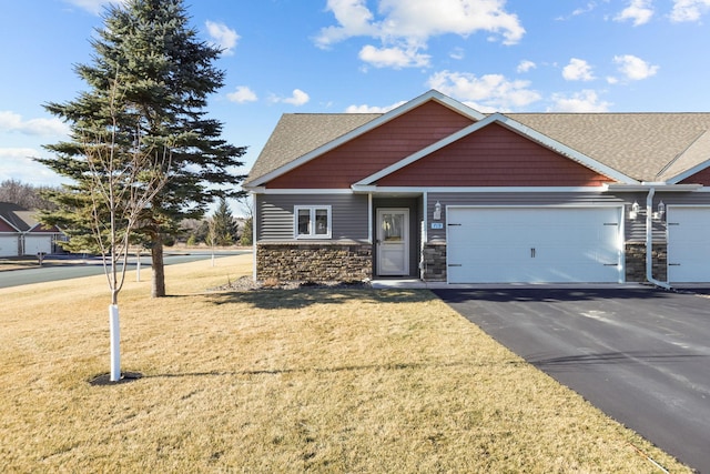 craftsman-style house with an attached garage, a front yard, aphalt driveway, and stone siding