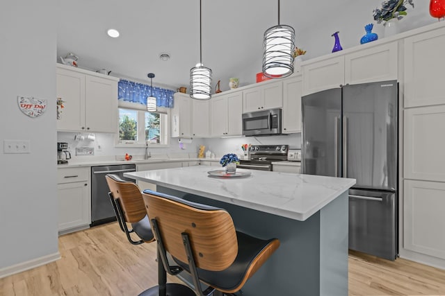 kitchen with white cabinets, stainless steel appliances, light wood finished floors, and a breakfast bar area