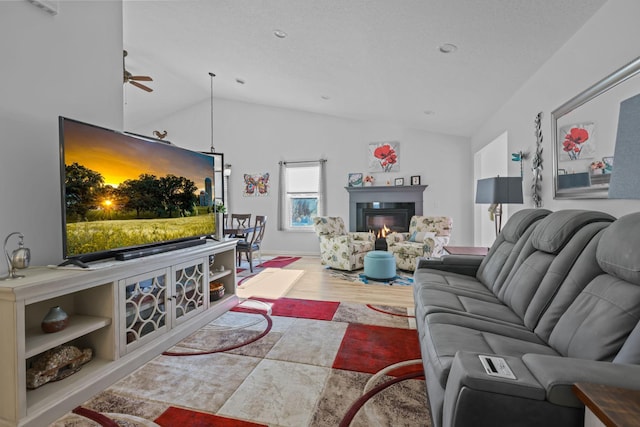 living room with ceiling fan, lofted ceiling, a glass covered fireplace, and wood finished floors