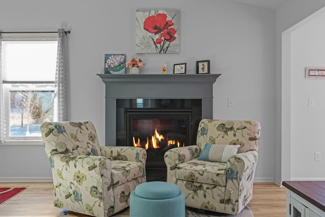 sitting room featuring baseboards, a glass covered fireplace, and wood finished floors