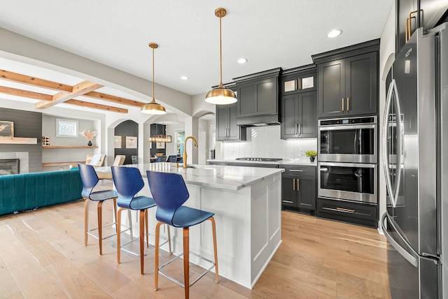 kitchen featuring sink, a breakfast bar area, a kitchen island with sink, stainless steel appliances, and decorative light fixtures