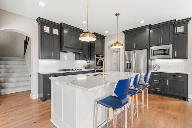 kitchen with sink, decorative light fixtures, an island with sink, stainless steel appliances, and light stone countertops