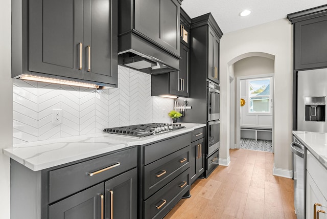 kitchen with appliances with stainless steel finishes, tasteful backsplash, light stone counters, a textured ceiling, and light wood-type flooring