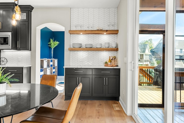 kitchen featuring hanging light fixtures, light hardwood / wood-style flooring, stainless steel microwave, and decorative backsplash