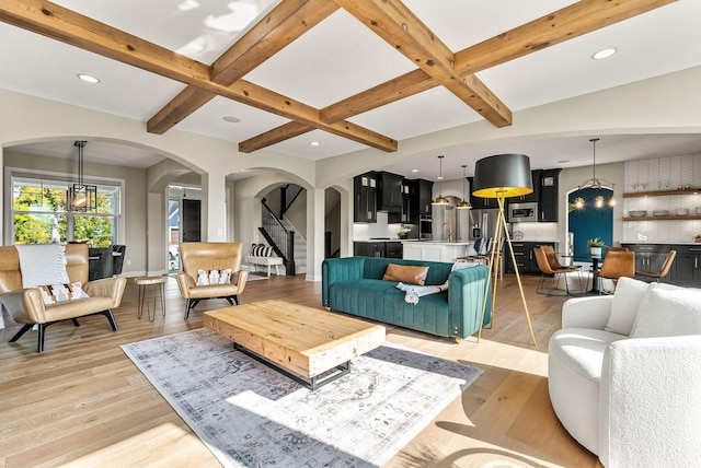 living room with coffered ceiling, light wood-type flooring, a notable chandelier, and beam ceiling