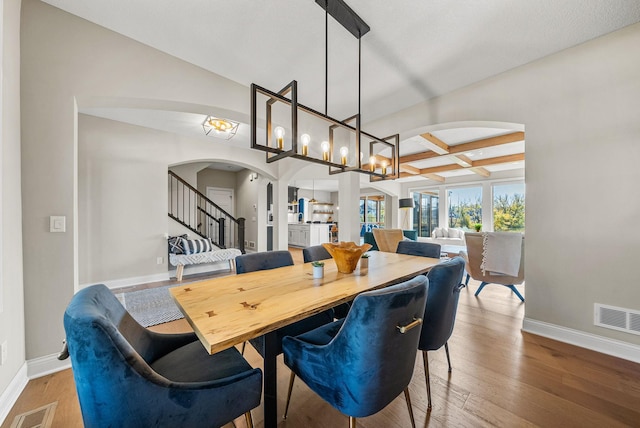 dining area featuring beamed ceiling, coffered ceiling, hardwood / wood-style floors, and a notable chandelier