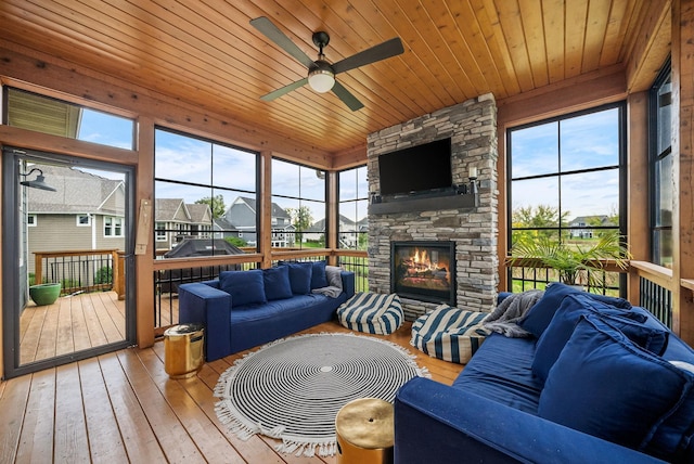 sunroom featuring ceiling fan, a stone fireplace, and wood ceiling