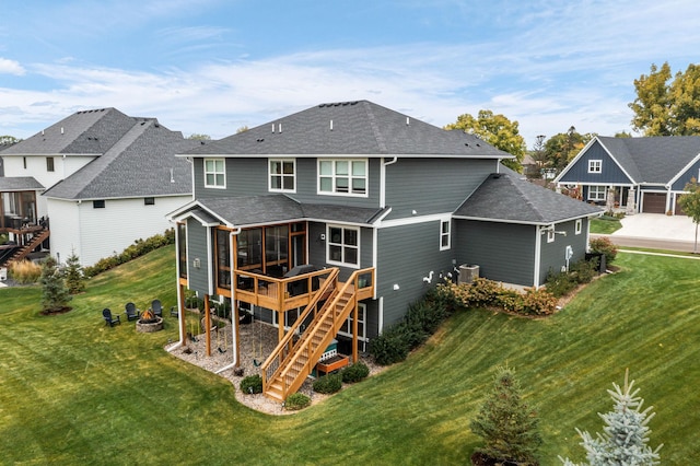 rear view of property with a fire pit, a wooden deck, a yard, and a sunroom