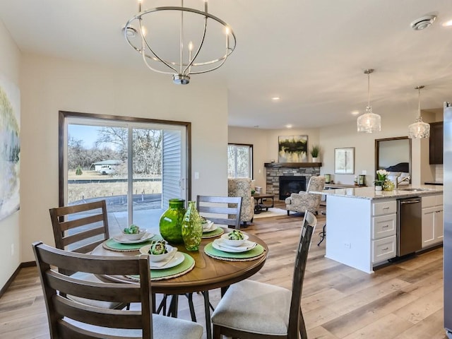 dining room featuring a fireplace, light wood-type flooring, a notable chandelier, and sink