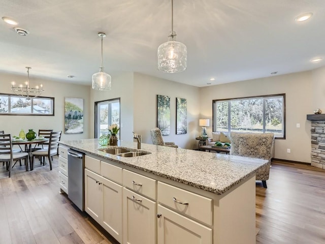 kitchen featuring pendant lighting, dishwasher, a kitchen island with sink, sink, and light stone countertops