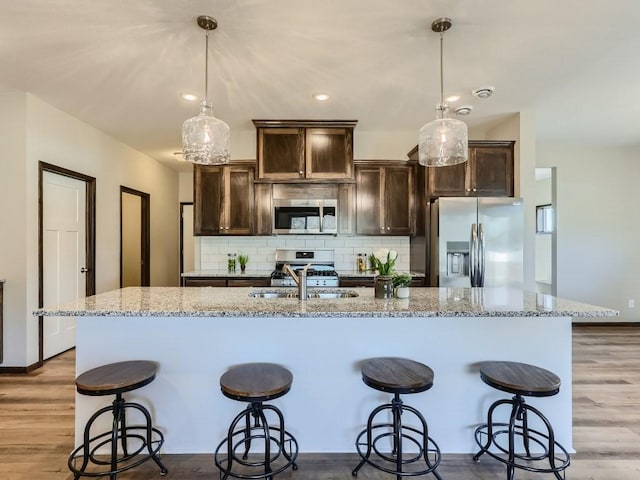 kitchen with decorative light fixtures, backsplash, stainless steel appliances, and a kitchen island with sink