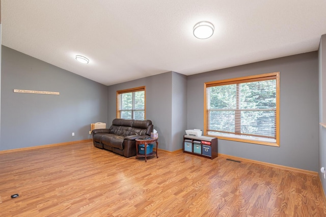 living area with a textured ceiling, light wood-type flooring, and lofted ceiling