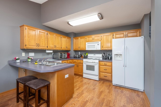 kitchen featuring white appliances, sink, light hardwood / wood-style floors, kitchen peninsula, and a breakfast bar area